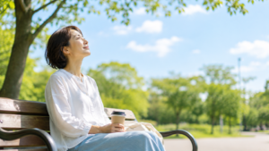 休日の昼下がり。日本人が公園のベンチでゆっくり空を見上げている。予定を詰め込まず、休むことを受け入れている