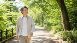 木漏れ日のある遊歩道をゆっくり歩く男性。表情は穏やかで前向き。青空と緑に囲まれ、自分のペースを取り戻した様子。