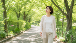 緑の遊歩道を女性が穏やかな表情で歩いている。周囲には柔らかな木漏れ日。自分のペースで進んでいる安心感を感じている