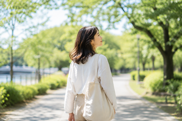 公園や緑の多い場所を一人でゆっくり歩く女性